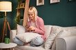© djile - Smiling young woman using smartphone while sitting cross-legged on sofa at home