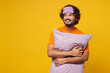 © ViDi Studio - Calm young Indian man wears orange pyjamas jam sleep purple eye mask rest relax at home hold pillow look aside on area isolated on plain yellow background studio portrait. Good mood night nap concept.