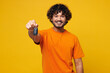 © ViDi Studio - Young smiling fun happy Indian man wear orange t-shirt casual clothes hold in hand car fob keyless system stretch arm to camera isolated on plain yellow background studio portrait. Lifestyle concept.