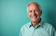 © miss irine - Happy senior man in blue-green shirt smiles at camera. Aged adult with grey hair poses on vibrant solid teal background with copy space. Portrait of a confident elderly man.