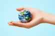 © Splash - A small earth globe resting on a child's open palm against a light blue background in a studio setting