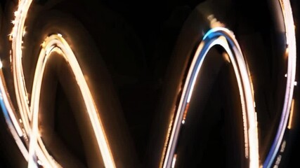 Poster - Light trails create a double arch shape against a dark background, resembling a stylized letter m or similar symbol, with variations in brightness and color