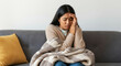 © Postmodern Studio - Young hispanic woman feeling unwell on couch with blanket