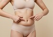 © PP Creative - A woman in light-colored underwear pointing at her belly, highlighting excess fat or loose skin with a focus on body awareness and fitness