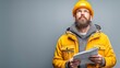 © Chanagun - A focused builder in a bright orange hat and jacket looks upward, holding blueprints. The image conveys determination and insight in construction and project planning.