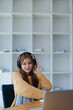 © Jirapong - Young woman enjoying a relaxing music break at her desk while using headphones, writing in a notebook, and working on her laptop for calm inspiration