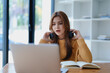 © Jirapong - Young woman enjoying a relaxing music break at her desk while using headphones, writing in a notebook, and working on her laptop for calm inspiration