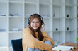 © Jirapong - Young woman enjoying a relaxing music break at her desk while using headphones, writing in a notebook, and working on her laptop for calm inspiration