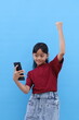 © ArvStd - Happy asian little girl standing while holding cell phone and clenching her hand. Isolated on blue