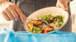 © sebra - Woman scraping leftover food from plate into trash bin in kitchen