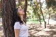 © Alina - Woman enjoying nature while resting against a tree in a sunny park setting