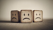 © Inspire Shots Hub - Three wooden cubes with sad faces, arranged on a wood surface, showing a concept of sadness or depression