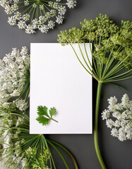 Aufkleber - White card stands on gray surface. Green plants surround card. Small green leaf rests on card. Background is muted and minimal. Delicate flowers shown.