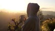 © Sia - Back view of hooded woman drinking a hot beverage while enjoying a breathtaking sunrise over a mountain range, creating a serene and inspiring moment. Concept morning in mountains with cup of coffee