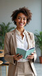 © Elena - Professional woman smiling while holding a book in a modern office