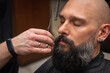 © Jurii - Close-up of a barber trimming a beard with electric clippers in a modern barbershop. Professional men's grooming and beard care service, selective focus