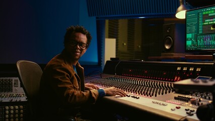 Leinwandbilder - Music producer operating mixing console in control room and working with audio recording software on pc, post production. Sound engineer editing tracks to produce new songs. Camera B.