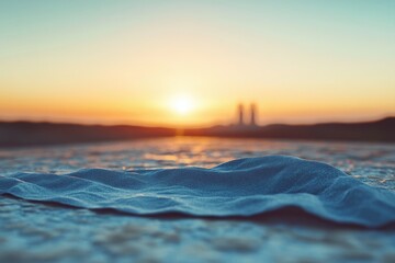 Poster - A textured blue cloth rests on a surface, with a blurred sunset and distant industrial structures in the background.