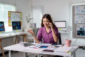 Poster - Asian businesswoman talking on phone and analyzing marketing data using laptop computer in office