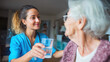 © Yuliia Litvinova - A compassionate nurse offers a glass of water to a senior patient, with a caregiver supporting in a nursing home, aiding elderly rehabilitation during retirement.
