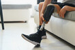 © Serhii - Man amputee with prosthetic leg disability on above knee transfemoral leg prosthesis wearing shoe sitting on sofa, close up. People with amputation disabilities everyday life concept