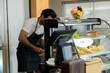 © Rakchanok - Multiethnic barista couple arms crossed smile looking camera happy start-up cafe small business entrepreneur, Indian worker teaching wife using technology system for order purchasing in coffee shop