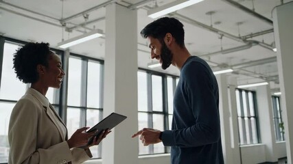 Poster - Two business colleagues, a woman and a man, are standing in a modern office, engaged in a discussion about a project while looking at a tablet