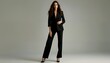 © KarpenArt Studio - a full-length studio shot of a woman in a black tailored suit and high heels posing against a muted green backdrop.