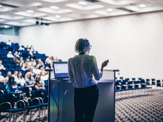 Wall Mural - female speaker giving a talk on corporate business conference. unrecognizable people in audience at 
