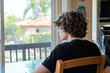 © Thanakit  - young person with curly hair sits table, gazing out window, lost thought. sunlight filters through glass, creating serene