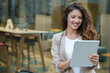 © Dorde - Confident Caucasian Businesswoman Smiling While Using Tablet in a Modern Urban Outdoor Setting
