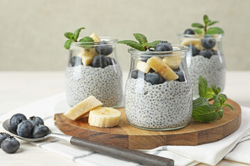 Wall Mural - Delicious chia pudding with blueberries, banana and mint in glasses on light table, closeup