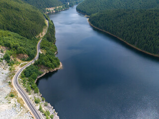 Fototapete - Aerial view of curved road alongside lush green forest and tranquil lake waters