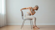 © Yury - Senior woman practicing gentle stretching while sitting on a chair in a bright indoor setting, promoting flexibility and wellness