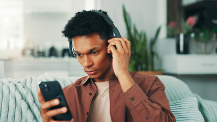 Poster - Headphones, phone and man on sofa in home listening to music, album or playlist for review. Serious, living room and person with cellphone and audio tech for streaming app with podcast in apartment.