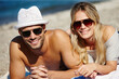 © peopleimages.com - Couple, sunglasses and relax on beach towel, smile and peace on vacation or lying by water. People, happy and tropical ocean for bonding on weekend, outdoor nature and love for marriage or romance