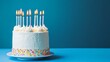 © touseef - White birthday cake with lit candles on blue background featuring frosted icing and colorful flame decorations, ideal for celebration themes, party invitations, and festive greeting designs with copy
