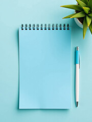 Aufkleber - A Simple Setup Featuring A Blue Notepad, Pen, And Greenery On A Pale Blue Background With Empty Space Nearby.
