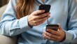 © natakot - A focused woman with long hair is engaged in multitasking, holding two smartphones in her hands while seated comfortably. This image captures the essence of modern connectivity and the fast-paced