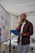 © Tj - Businessman holding a clipboard and pen, reviewing charts and graphs on a whiteboard, demonstrating focused analysis of business performance in a meeting