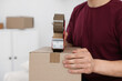 © New Africa - Man using dispenser with adhesive tape to seal cardboard box indoors, closeup