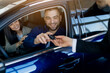 © Anastasiya - Smiling millennial couple receiving car keys from salesman while sitting inside their newly purchased car in dealership showroom, happy spouses buying modern vehicle in auto salon, closeup