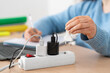© cunaplus - Female student hand plugging plug on a power strip socket using laptop on a desk at home