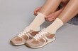 © New Africa - Woman in stylish beige socks and sneakers on light grey background, closeup
