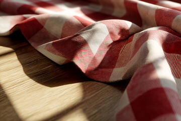 Fototapete - Red and white checkered fabric draped on wood surface, illuminated by sunlight, showcasing texture and folds, suggesting warmth and rustic charm, ideal for background use