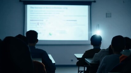 Poster - This group of students focuses on a presentation screen in a dimly lit classroom.