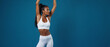 © schiers_images - Strong and confident woman modeling white activewear while striking a pose, showcasing fitness and health. The vibrant blue backdrop emphasizes her figure and symbolizes energy and balance.