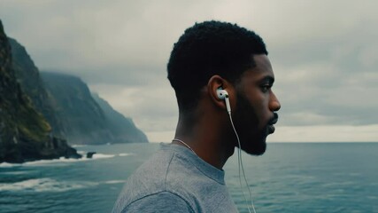 Poster - A person wearing earphones stands at the edge of the ocean, looking out at the waves.