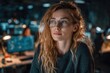 © whitestorm - A beautiful, thoughtful young woman with curly hair in glasses looking at computer screen, reflecting the glow, sitting in a modern, busy office environment at night.