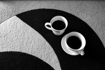 Poster - High angle shot of two coffee cups on a black and white patterned surface, offering a modern, minimalist aesthetic with a focus on contrast and simple elegance.